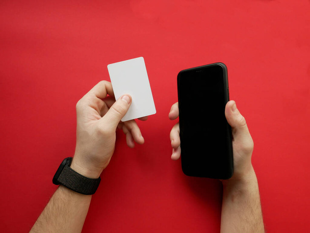 Käsi älykäs katsella tilalla valkoinen kortti ja älypuhelin punaisella taustalla. Käteismaksu, verkko-ostoksia. Yläkuva
. - Valokuva, kuva