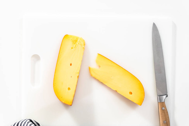 Large slice of smoked gouda cheese on a white cutting board. - 写真・画像