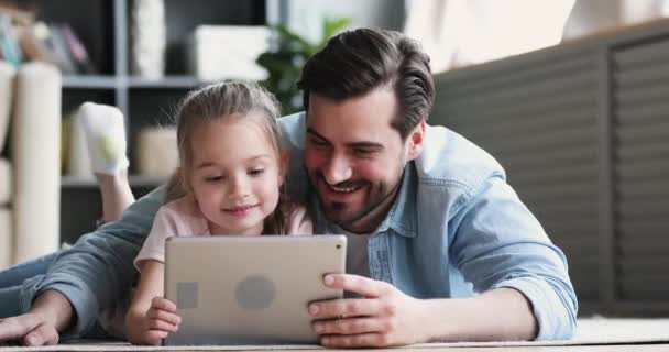 Dad and small daughter using digital tablet lying on floor - Video