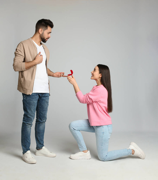 Young woman with engagement ring making marriage proposal to her boyfriend on light grey background - 写真・画像