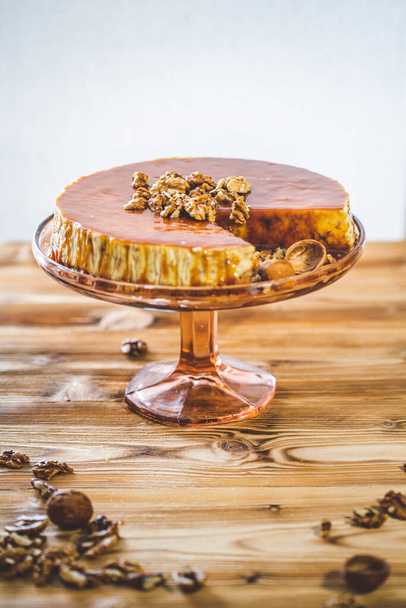 Chessecake casero dulce con cobertura de caramelo y nueces de nuez en la mesa de madera. Sabroso postre de pastel marrón
. - Foto, Imagen
