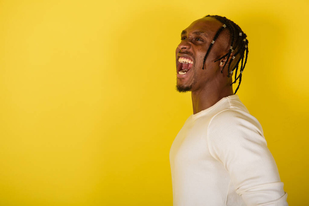 portrait of a young black man, african appearance, emotional and serious and looking upwards, flailing his hands, from dreadlocks, against yellow background  - Zdjęcie, obraz