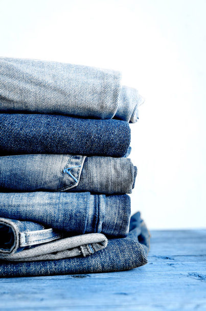 Classic blue color jeans stacked on a wooden table. Denim textiles clothing background pile concept. Classic blue color of the year 2020 concept. Copy space. - Photo, Image