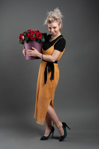 Stüdyoda çiçek açan çiçeklerle dolu bir sepeti tutan güzel sarışın, beyaz bir kadın. - Fotoğraf, Görsel
