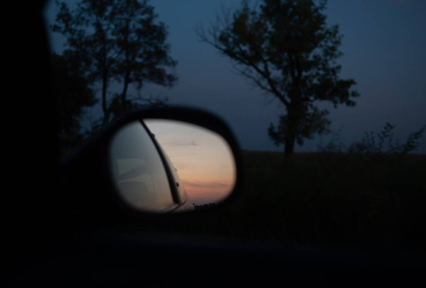 Réflexion du coucher de soleil dans le rétroviseur latéral de la voiture. Lorsque vous voyagez sur une autoroute, le reflet d'un camion semi-remorque sur le rétroviseur droit d'un VUS pendant le coucher du soleil
. - Photo, image