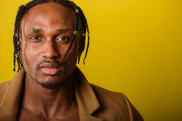 portrait of young black man, african appearance, emotional and serious and looking straight, with dreadlocks, against yellow background  - Photo, Image