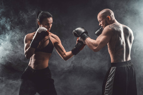 Shirtless Woman exercising with trainer at boxing and self defense lesson, studio, smoke on background. Female and male fight - Фото, зображення