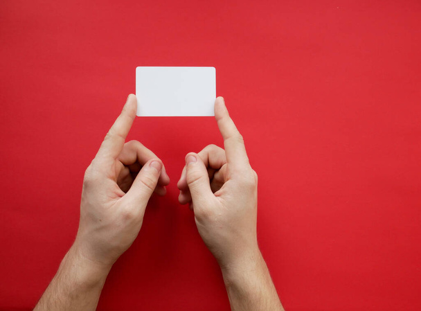 Mãos femininas segurando cartão branco branco branco no fundo vermelho. Vista superior
 - Foto, Imagem