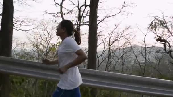Yoldaki tepede koşan Asyalı kadın. Dişi koşucu yaz boyunca tropikal ormanlar arasında dağa tırmanmayı hedefliyor. Yavaş çekim. - Video, Çekim