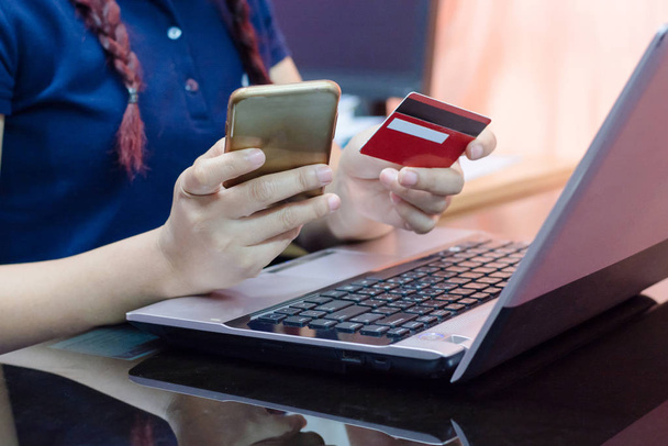 Manos de mujer sosteniendo la tarjeta de crédito utilizando en el teléfono inteligente y portátil. concepto de compras en línea.Pago en línea
 - Foto, Imagen