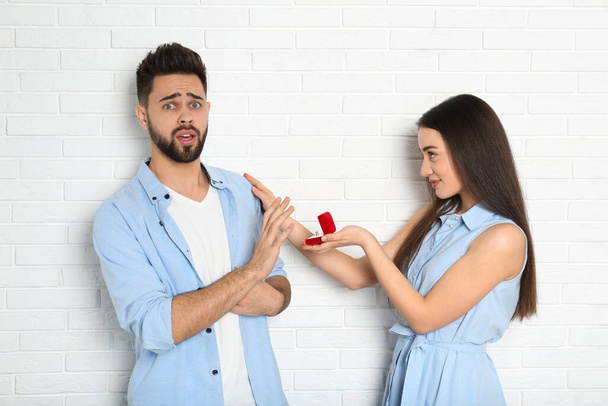 Young man rejecting engagement ring from girlfriend near white brick wall - Photo, image