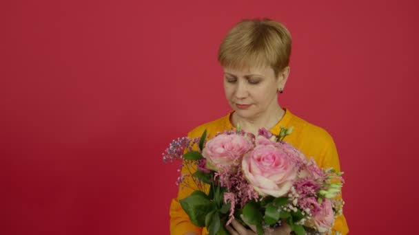 Mulher madura segurando bouquet eustoma e cheirando flores com sorriso
 - Filmagem, Vídeo