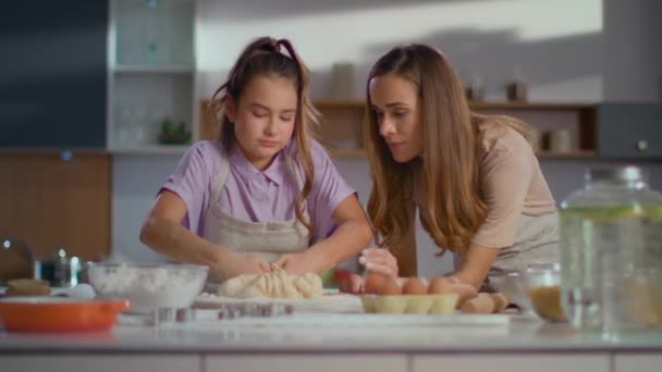 Mujer atractiva enseñando a chica a preparar masa para galletas en la cocina moderna
 - Metraje, vídeo