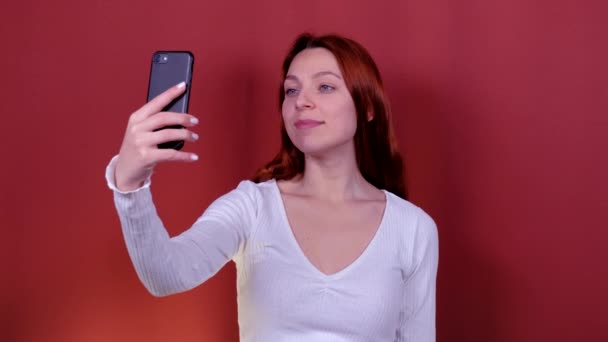 Een jonge vrouw met rood haar neemt een selfie met haar telefoon. - Video