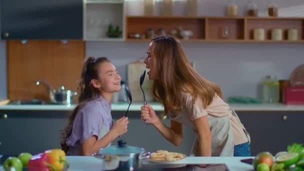 Смішна дівчина і жінка співають ложки на сучасній кухні в повільному русі
 - Кадри, відео