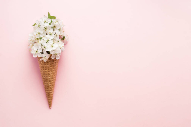 薄ピンク色のパステルカラーの背景に白い桜の花とワッフル甘いアイスクリームコーンのフラットレイ。春のムードを最小限の概念。最上階だ。スペースのコピー. - 写真・画像