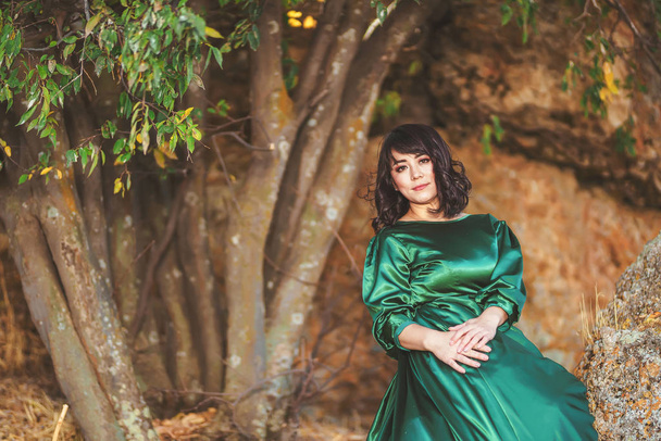 Woman in  lush green dress in early autumn in Aksu canyon in southern Kazakhstan. Young woman in fairy tale evening ball gown on background of rocks. Beautiful girl in long dress in the mountains - Фото, изображение