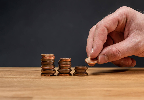 Eine Hand stapelt Münzen auf einem Holztisch vor dunklem Hintergrund. - Foto, Bild