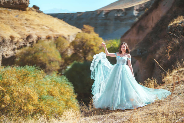 Женщина в пышном красивом мятном платье в каньоне Аксу на фоне реки на юге Казахстана. Молодая женщина в вечернем бальном платье на фоне скал и гор. Красивая девушка в длинном воздушном платье в горной местности
 - Фото, изображение