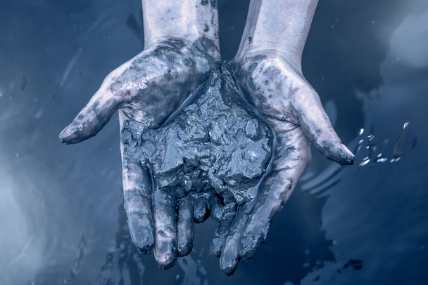 Las manos de las muchachas sostienen lodo del Mar Muerto que tienen propiedades curativas en el Mar Muerto, Israel. Tonificación azul
. - Foto, Imagen