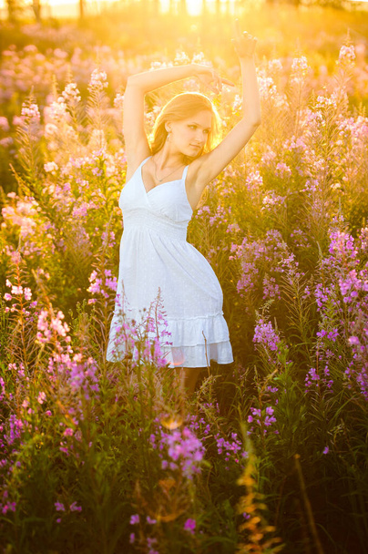 A fiatal, gyönyörű szőke lány rózsaszín virágokat gyűjt a tavaszi virágzó mezőn naplementekor. A szépség, frissesség, ifjúság és egészség fogalma a természetes kozmetikumok reklámozására. - Fotó, kép