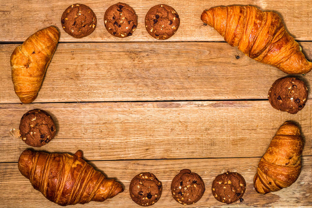 Φρέσκο κρουασάν, σφολιάτα και μπισκότα σε ξύλινο τραπέζι. Έννοια φαγητού και πρωινού. Γλυκά και φρέσκα γλυκά. Κάτοψη και αντίγραφο χώρου - Φωτογραφία, εικόνα
