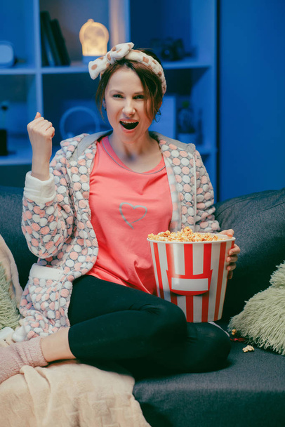 Happy beautiful girl face watching comedy film in home. Millennial woman sitting on sofa and watching TV. Concept of entertainment. Positive emotions - 写真・画像