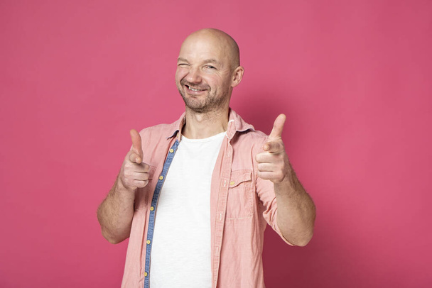 Retrato de um homem sorrindo positivo com restolho, apontando com dois dedos indicador para a câmera e olhando com os olhos espremidos
 - Foto, Imagem
