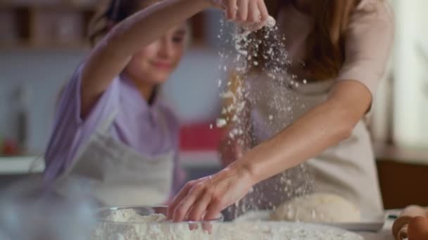 Woman and girl sprinkling flour on table at kitchen in slow motion - Video, Çekim