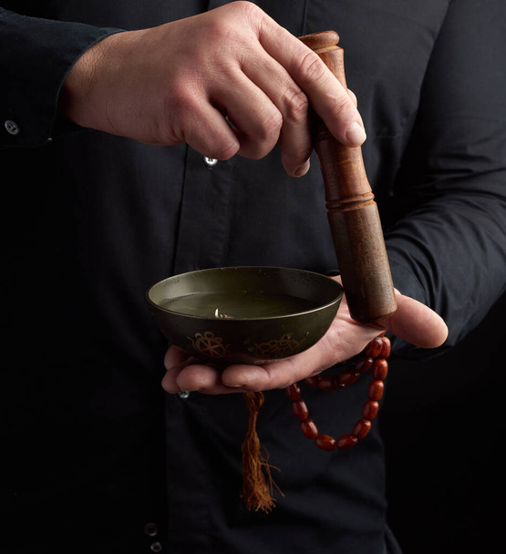 adult man in a black shirt rotates a wooden stick around a copper Tibetan bowl. ritual of meditation, prayers and immersion in a trance. Alternative treatment - 写真・画像