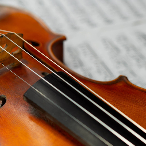 Schöne alte Geige in Großaufnahme auf dem verschwommenen Notenblatt liegend - Foto, Bild