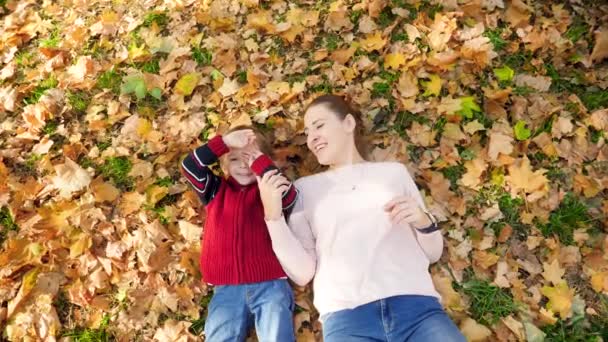 4k vídeo de feliz sorrindo e rindo menino com a jovem mãe deitada na grama e folhas no parque de outono
 - Filmagem, Vídeo