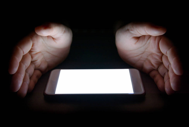 valkoinen valo älypuhelimesta heijastavat kättäsi yöllä pimeässä ruudussa tekstiä ja suunnittelua varten
 - Valokuva, kuva