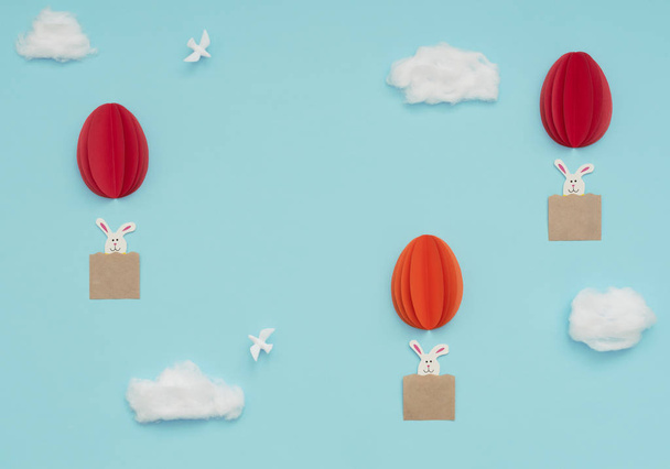Velikonoční vajíčka horkovzdušné balónky z papíru s králíčky létají na modré obloze s bavlněnými mraky a bílými holubicemi. Veselé Velikonoce. Pozdrav. Plochý styl s kopírovacím prostorem.  - Fotografie, Obrázek