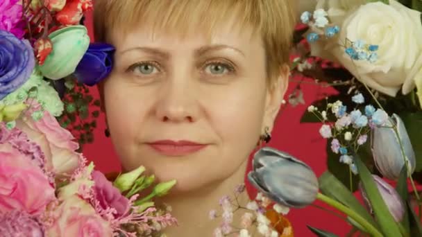 Első nézet érett nő virágokkal nézi kamera mosollyal - Felvétel, videó