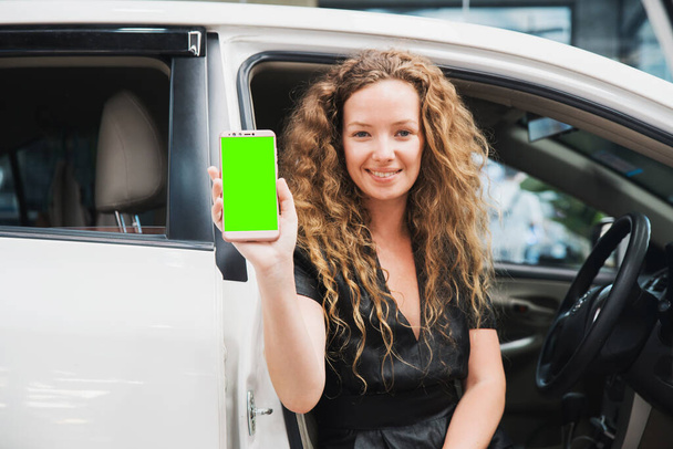 Kobieta siedząca w samochodzie i pokazująca swój smartfon z zielonym ekranem. Aplikacja samochodowa. Auto Leasing Biznes. Biznes cyfrowy. - Zdjęcie, obraz