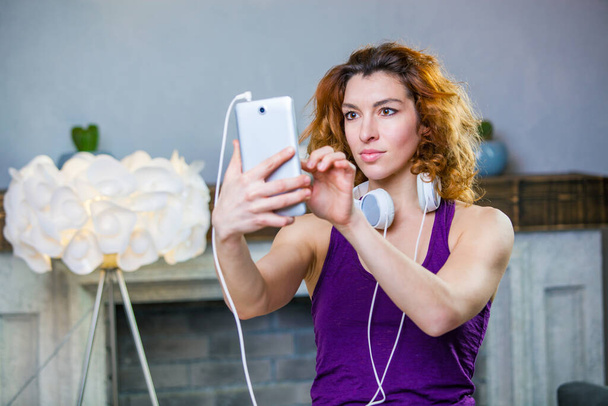 Portrait of an attractive woman with headphones on and holding smartphone in her hands choosing music - Fotografie, Obrázek