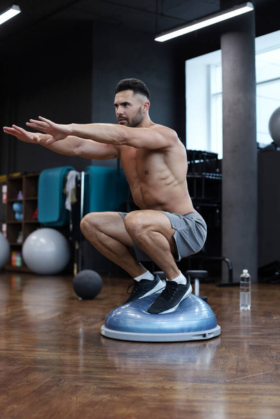 Fit athlete performing exercise on gymnastic hemisphere bosu ball in gym - Foto, immagini