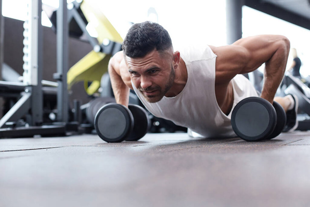 Fit and muscular man doing horizontal push-ups with dumbbells in gym - Foto, imagen