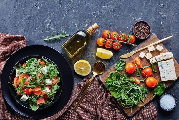 salmon arugula blue cheese tomato salad in a black bowl  with brown cloth and ingredients, horizontal view from above, flat lay, free space - Foto, immagini
