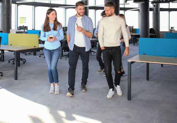 Longitud completa de los jóvenes en ropa casual inteligente discutiendo negocios y sonriendo mientras caminan por la oficina
 - Foto, Imagen