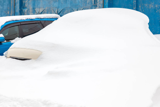 Autók egy parkolóban a hó alatt, egy kék kerítés mellett. Járművek elkobzása. Nyaralás koncepció a forró országokban egy autó parkolt hosszú ideig a télen. - Fotó, kép