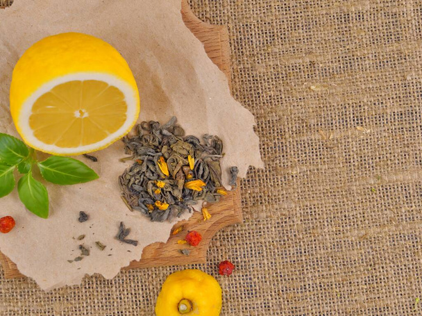 Half a yellow lemon, dry green tea, mint leaves on a burlap background. - Photo, image