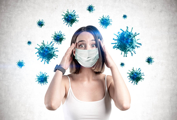 Scared young woman in protective mask standing near concrete wall with blue viruses around her. Concept of coronavirus Asian flu panic - Photo, Image