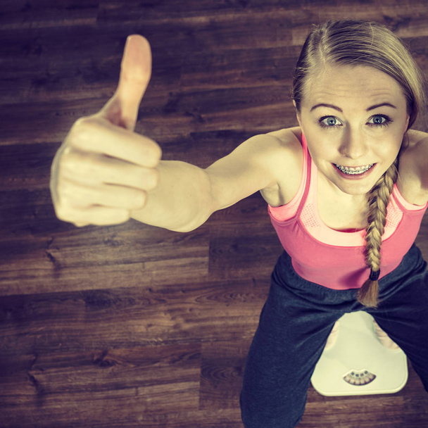 Teenage woman on bathroom scale machine thinking about weight loss and proper body mass showing thumb up gesture. Being fit and healthy concept. - Foto, Bild