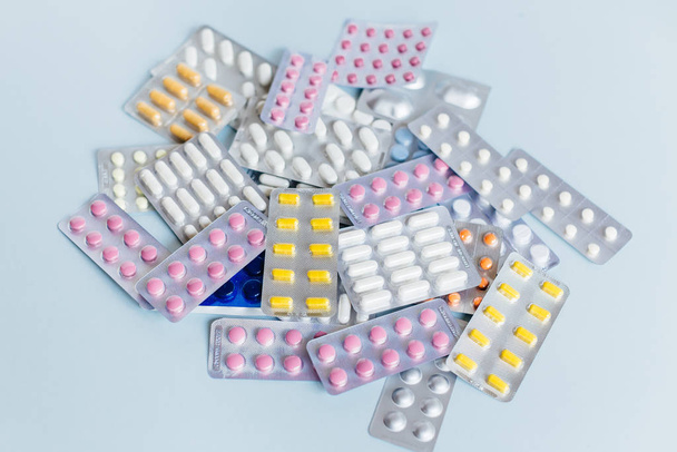 Verschiedene Medikamente: weiße, rosa und gelbe pharmazeutische Medikamentenpillen, Mittel gegen Grippe, Kopfschmerztabletten, Antibiotika. Medizin- und Gesundheitskonzept. Weicher Fokus, blauer Hintergrund. - Foto, Bild