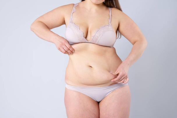 Tummy tuck, flabby skin on a fat belly, plastic surgery concept on gray background - Fotó, kép