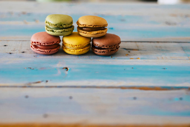 Mesa de madera azul con cinco sabrosos macarrones coloreados - primer plano de la comida de panadería
  - Foto, Imagen
