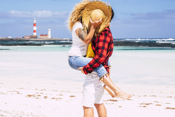 Couple kissing with love - concept of summer holiday vacation or honeymoon for people in relationship - background with beach and blue ocean and sky - man carry woman with curly hair - Fotó, kép