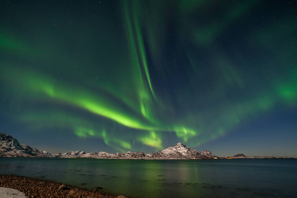 zelená aurora borealis na okraji moře s záblesky měst v zasněžené krajině a ostré hory, dlouhá doba závěrky. - Fotografie, Obrázek
